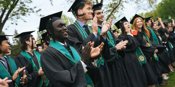 students applaud while wearing caps and gowns