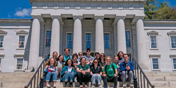 A group of students and staff pose for a photo on the steps of the Vermont State House.