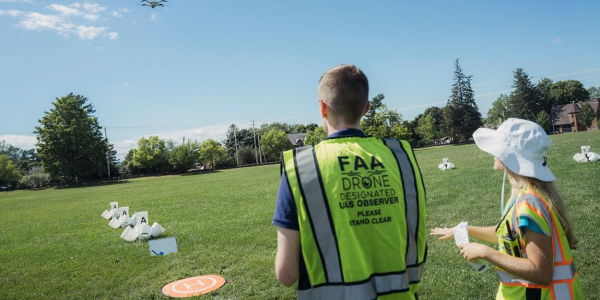 A participant in the UVM drone training workshop being led through a flight training proficiency test outside on a campus green.